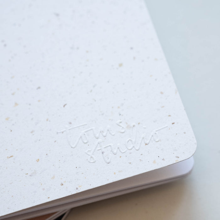 Detail of embossed logo on Tom's Studio x Coffeenotes A6 Notebook in 'Grounds' (white), made from recycled coffee cups and eco-friendly materials.