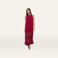 A woman is wearing the Adalynn Cover-Up Dress, a sleeveless, ankle-length red chiffon getaway dress featuring a pleated top and lace details at the hem, while standing barefoot against a plain white background.