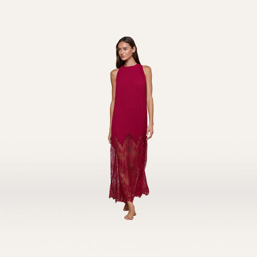 A woman is wearing the Adalynn Cover-Up Dress, a sleeveless, ankle-length red chiffon getaway dress featuring a pleated top and lace details at the hem, while standing barefoot against a plain white background.