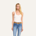 Woman with long blonde hair wearing the Adira Scoopneck Tank in white, styled in a slim fit with blue jeans, a brown belt, and hoop earrings stands facing forward against a plain light background.