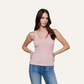 A woman with long brown hair wearing the Adira Scoopneck Tank in light pink and blue jeans stands with one hand on her hip, posing against a plain off-white background.