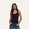 A woman with long dark hair wears the Adira Scoopneck Tank in navy blue and blue jeans, standing against a plain light background, looking at the camera with a neutral expression.