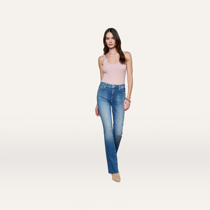 A woman stands facing forward against a plain white background, wearing the Adira Scoopneck Tank in light pink, blue bootcut jeans, and beige shoes.
