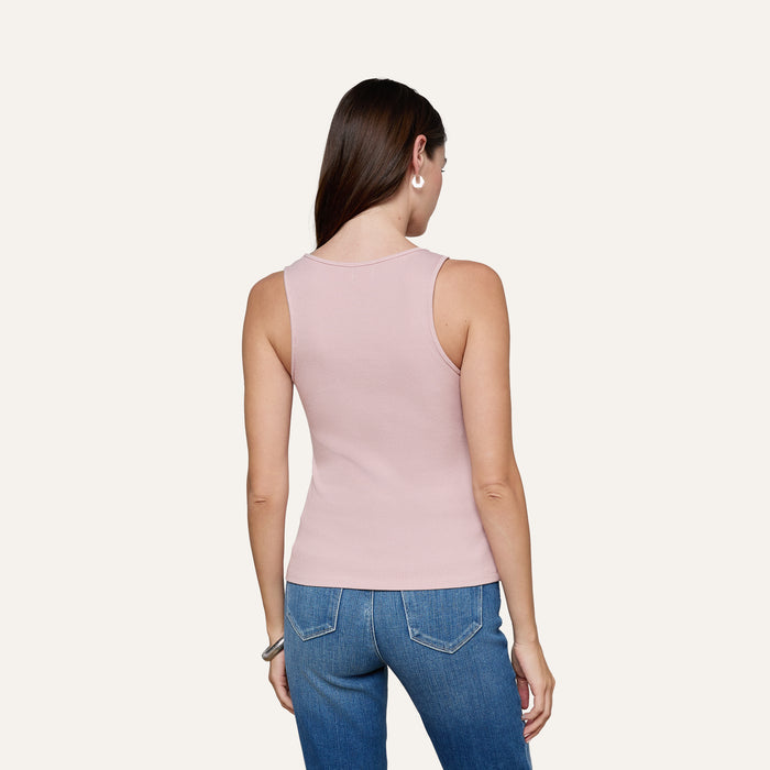 A woman with long brown hair stands facing away, wearing the Adira Scoopneck Tank in light pink and blue jeans against a plain light background.