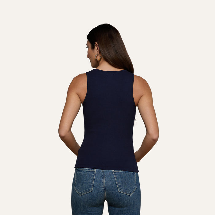 A woman with long dark hair, wearing the Adira Scoopneck Tank and blue jeans, stands facing away from the camera against a plain light background.