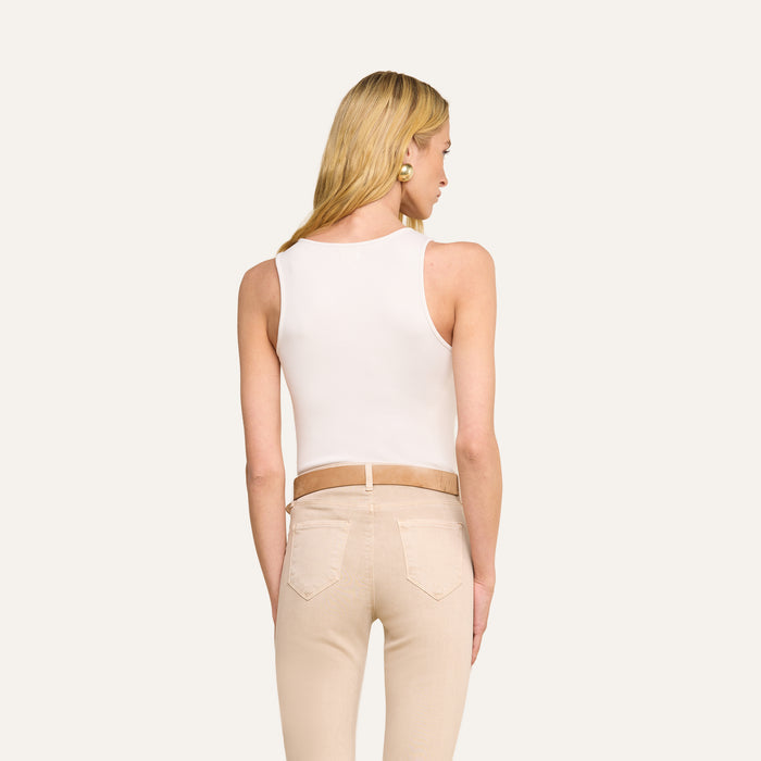 A woman with long blonde hair is shown from the back, wearing the Adira Scoopneck Tank in white along with beige pants and a tan belt, standing against a plain light background.