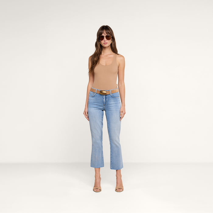 A woman wearing sunglasses, the Adira Tank in tan—a scoopneck sleeveless essential with a sculpted fit—light blue cropped jeans, a belt, and heeled sandals stands against a plain white background.