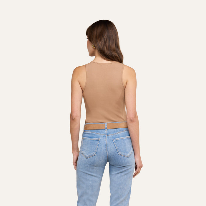 A woman with brown hair, wearing the Adira Tank in a sculpted fit paired with light blue jeans, stands facing away from the camera against a plain, light background.
