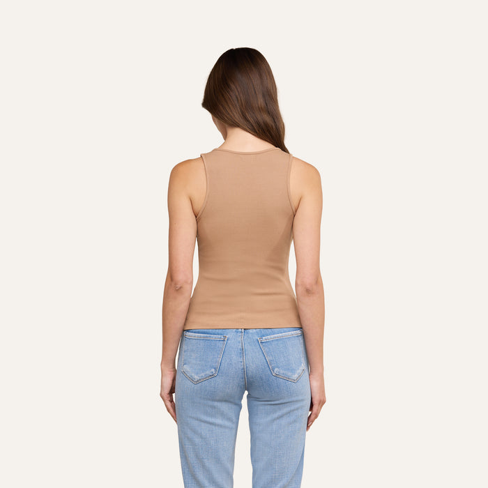 A person with long brown hair is standing facing away from the camera against a plain, light background, wearing the Adira Tank in a sculpted fit and light blue jeans.