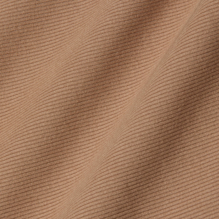 Close-up of the Adira Tank’s light brown ribbed fabric, with diagonal folds and fine textured lines that highlight the intricate pattern and soft surface of this essential piece.