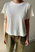 Person wearing a plain white t-shirt and green pants against a neutral background