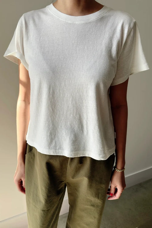 Person wearing a plain white t-shirt and green pants against a neutral background