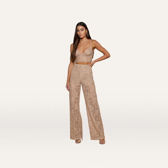 Woman wearing the Aislin Lace Bralette, a sleeveless beige crop top crafted from sheer stretch lace with scalloped edges, paired with matching high-waisted, wide-leg pants and open-toe heels, posing against a plain white background.