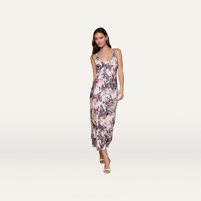 A woman stands facing forward against a plain white background, wearing the Akiya Satin Maxi Dress—a sleeveless, light pink, bias-cut satin dress featuring a vibrant butterfly jungle print.