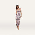 A woman stands facing forward against a plain white background, wearing the Akiya Satin Maxi Dress—a sleeveless, light pink, bias-cut satin dress featuring a vibrant butterfly jungle print.
