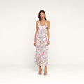 A woman stands against a plain background wearing the Akiya Satin Maxi Dress—a sleeveless, long, bias-cut satin dress adorned with pink and green floral patterns—paired with open-toe heels. This versatile day-to-night dress transitions effortlessly from casual outings to evening events.