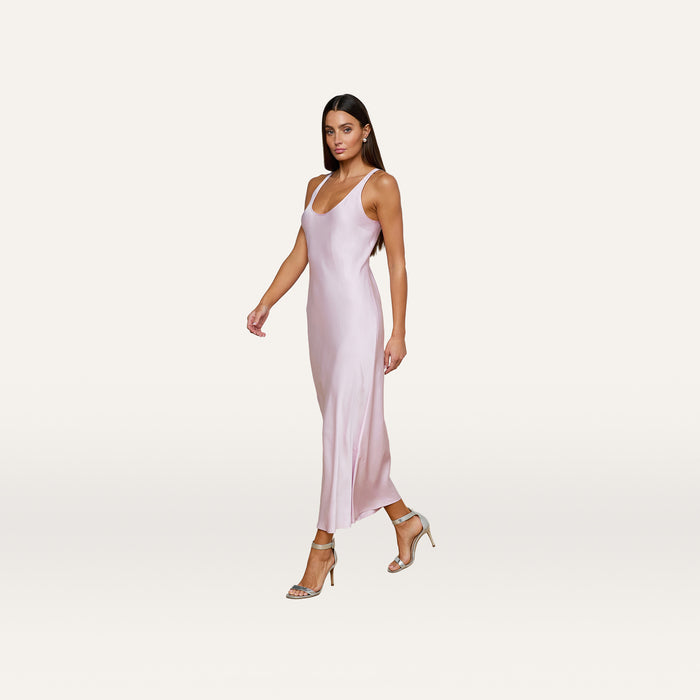 Wearing the Akiya Satin Maxi Dress in a sleeveless, pastel lilac design, a woman in strappy heels walks confidently against a plain, light background.