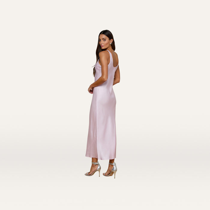 A woman in the Akiya Satin Maxi Dress, featuring a long, bias-cut silhouette in pastel lilac, stands on a plain white background in silver high heels, facing slightly to the side and looking toward the camera.