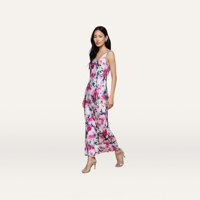 A woman wears the Akiya Satin Maxi Dress, a sleeveless, long pink dress adorned with pink and purple rose prints, standing in heels against a plain white background.