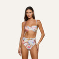 A woman stands against a plain white background, facing forward with a relaxed expression, wearing the Alexandria Bikini Top—a colorful, high-waisted bikini set featuring a postcard print and offering UPF 50 protection through its balconette-style design.