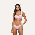 A woman stands facing forward against a plain light background, wearing the Alexandria Bikini Top—an underwire balconette bikini top crafted from textured pink and white bouclé fabric with gold buttons.