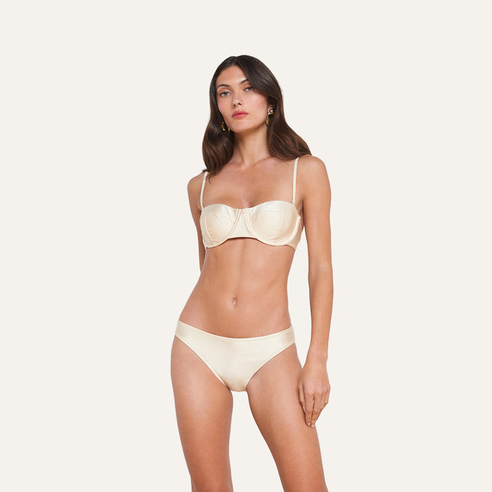 A woman wearing the Alexandria Bikini Top in cream with matching bottoms, standing against a plain light background, posed with a relaxed posture and neutral expression.