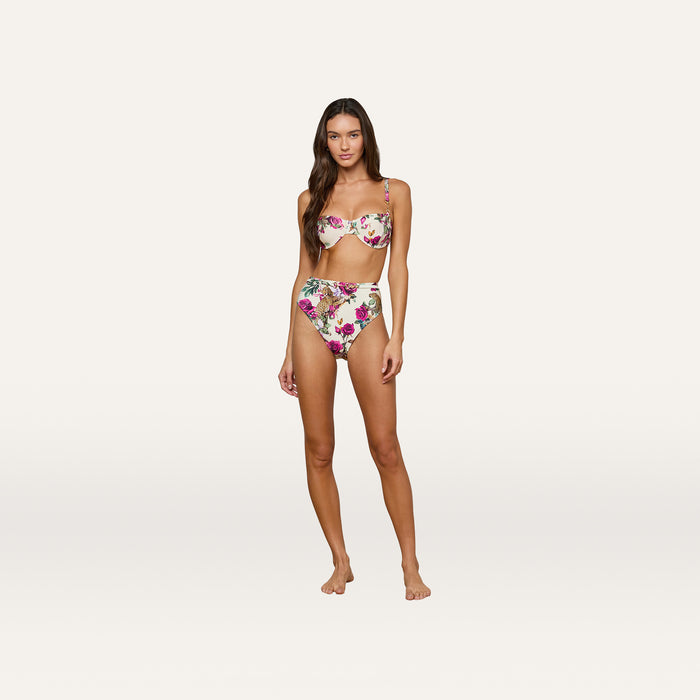 Woman standing against a plain background, looking at the camera with a neutral expression, wearing the Alexandria Bikini Top in a rose leopard print paired with high-waisted bikini bottoms.