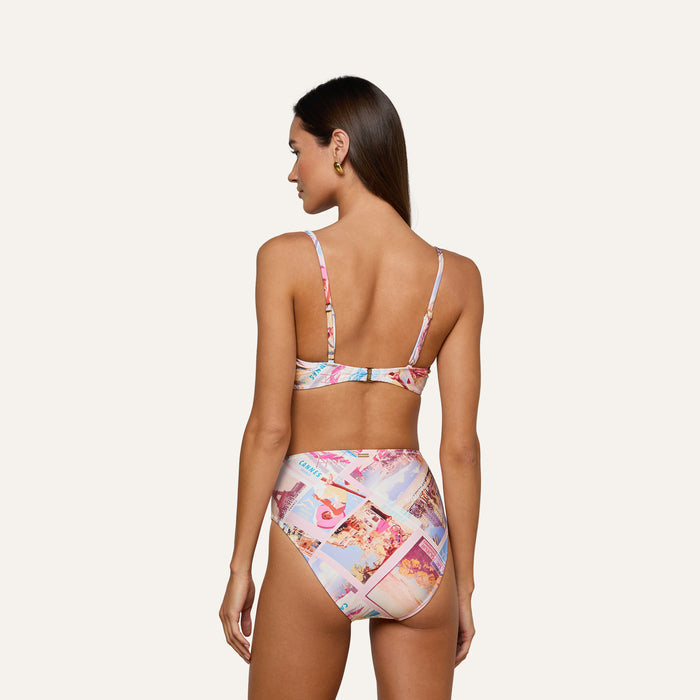 Woman with long brown hair, seen from the back and standing against a plain light background, wearing the Alexandria Bikini Top—a colorful, balconette swim top in a high-waisted bikini set featuring postcard print.