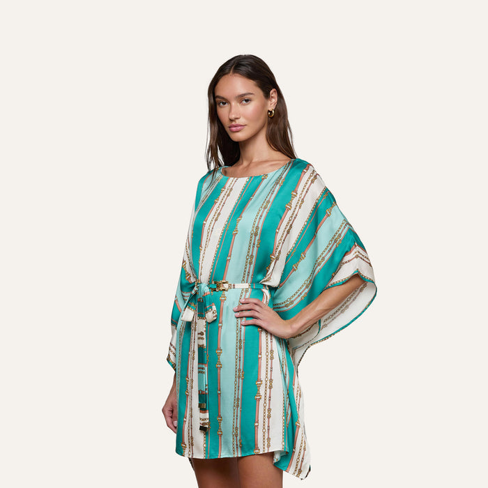 Woman wearing the Alia Cover-Up Tunic, featuring a turquoise and white belt-stripe print with gold accents, standing against a plain background.