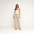 A woman wearing sunglasses, a beige tank top, and the Alicent Wide-Leg Jean with a belt stands in front of a plain white background. She completes her look with heeled sandals.