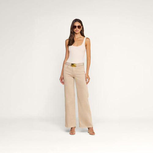 A woman wearing sunglasses, a beige tank top, and the Alicent Wide-Leg Jean with a belt stands in front of a plain white background. She completes her look with heeled sandals.
