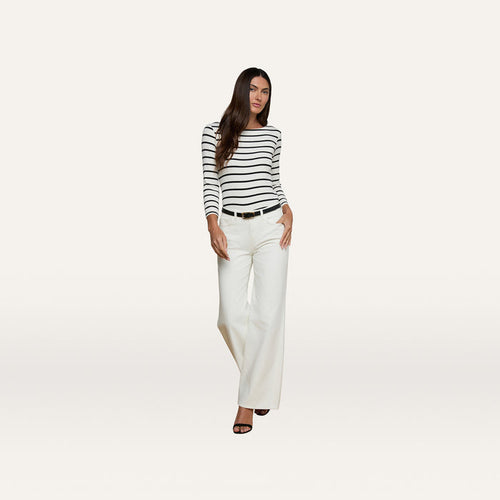 A woman stands against a plain background, wearing a black and white striped long-sleeve top, high rise Alicent Wide-Leg Jeans in white, a black belt, and black heels.