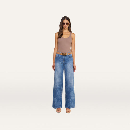 Woman standing against a plain background, wearing sunglasses, a taupe tank top, the Alicent Wide-Leg Jean—an all-cotton, sneaker-length denim style with a subtle floral print—paired with a tan belt and open-toe heels.