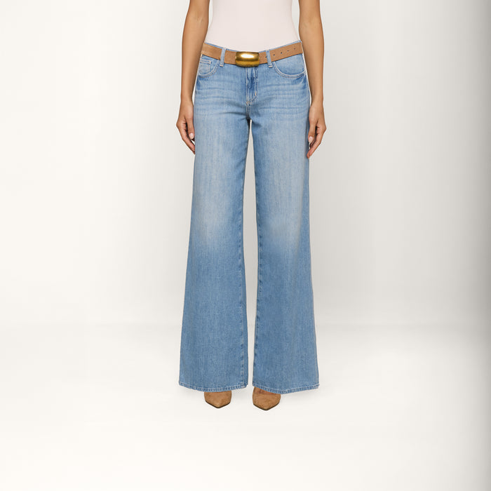 A person wearing the Alicent Wide-Leg Jean in light blue stands against a plain white background. The high rise, featherweight denim jeans feature a wide-leg silhouette and are styled with a brown belt and tan pointed-toe shoes. The upper body is cropped out of the frame.