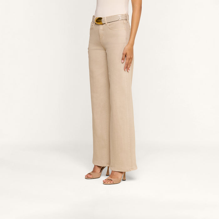 A person wearing the Alicent Wide-Leg Jean in beige—crafted from stretch denim with a matching belt—and open-toe heels, standing against a plain, light background.