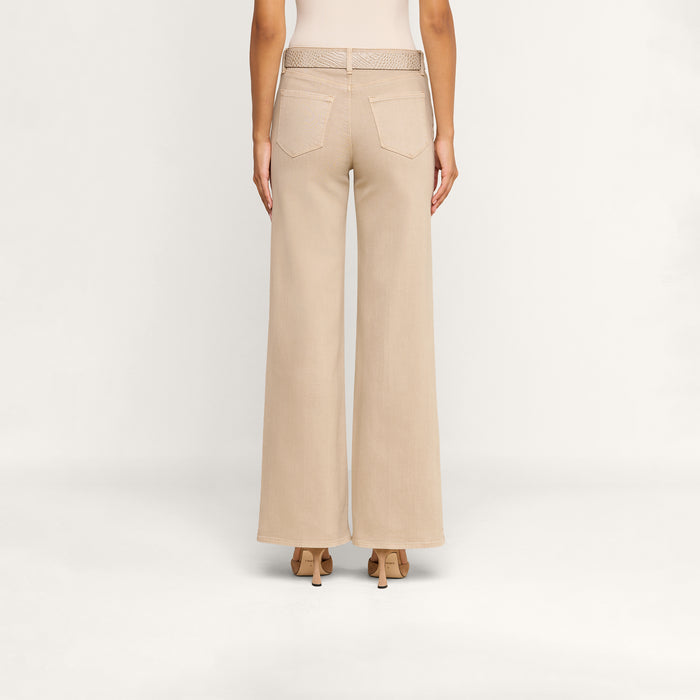 A person stands facing away against a plain white background, wearing the Alicent Wide-Leg Jean in beige with a matching belt and high-heeled shoes.
