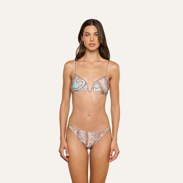 A woman stands against a plain background wearing the Alisha Bikini Top, a matching paisley-patterned swim separate featuring thin straps and a V-neck design. Her arms rest at her sides and she has a neutral expression, highlighting the stylish bikini top.