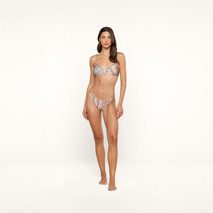 A woman stands on a plain white background, wearing the Alisha Bikini Top and matching bottoms with a colorful pattern and UPF 50 protection, looking straight at the camera with her arms relaxed by her sides.