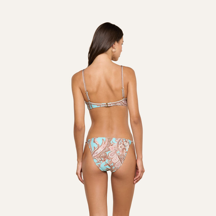 A woman stands with her back to the camera, modeling the Alisha Bikini Top—a swim separate featuring a blue and brown paisley pattern—set against a plain light background.