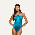A woman stands with her hands on her hips against a plain light background, wearing the Althea Bandeau One-Piece Swimsuit in shiny turquoise with pavé rhinestone accents.
