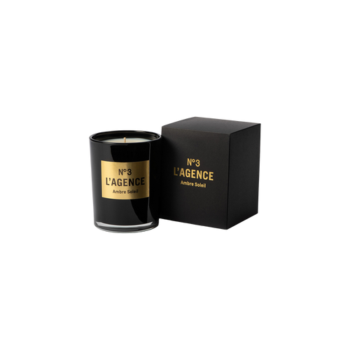 A black Ambre Soleil candle, crafted from soy-blend wax and adorned with a gold accent, sits beside its matching black and gold box on a plain white background.