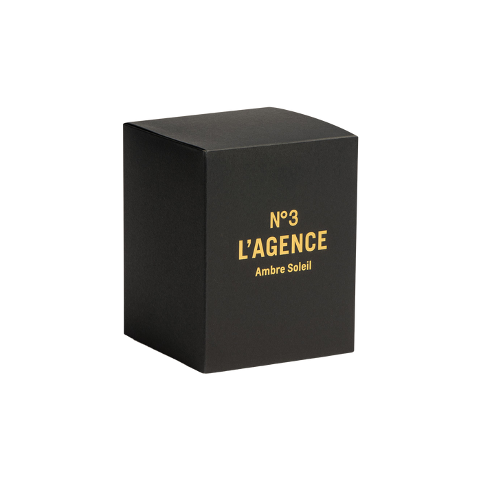 A sleek black box featuring gold lettering that reads “Ambre Soleil” stands against a crisp white background. The sophisticated packaging alludes to the luxury inside: hand-poured candles made from premium soy-blend wax, scented with the signature Ambre Soleil fragrance.