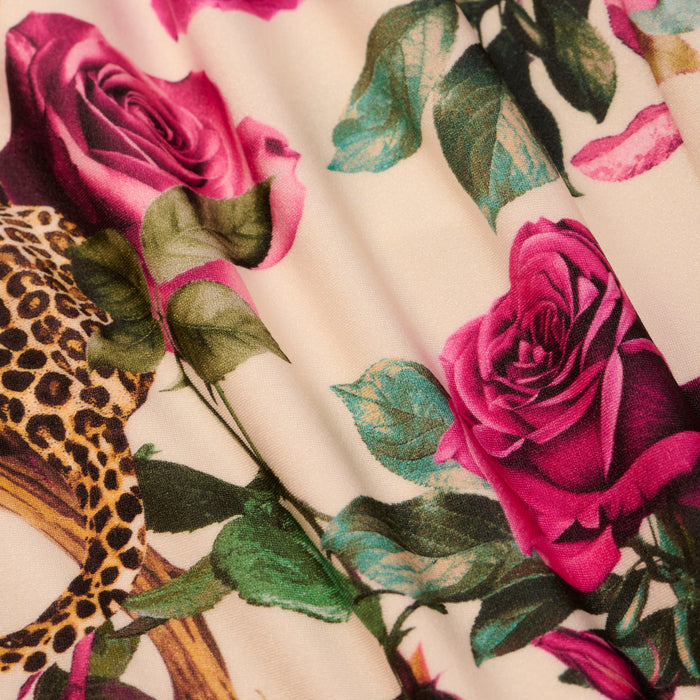 A close-up of the Amie Bandeau One-Piece Swimsuit showcases a vivid print of pink roses, green leaves, and a touch of leopard pattern on a light background.