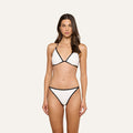 A woman stands facing forward, wearing the Annabelle Bikini Top—a white triangle silhouette bikini top with black trim and an adjustable fit. She has long brown hair and a neutral expression, posed against a plain light background.