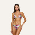 A woman poses in the Annabelle Triangle Bikini Top, featuring pink and purple flowers on a white background, against a plain light backdrop.