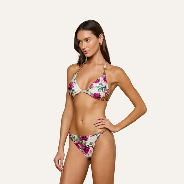 Wearing the Annabelle Triangle Bikini Top with pink and green floral patterns, a woman poses against a plain light background, standing with one hand on her hip and a neutral expression.