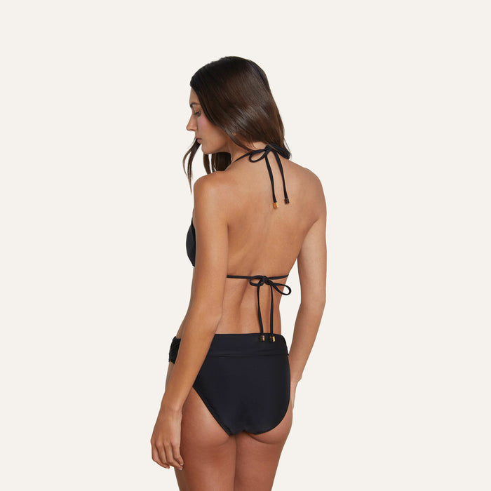 A woman with long brown hair is shown from the back, looking over her shoulder, wearing the Annabelle Triangle Bikini Top in black. The top features adjustable straps and is set against a plain, light-colored background.