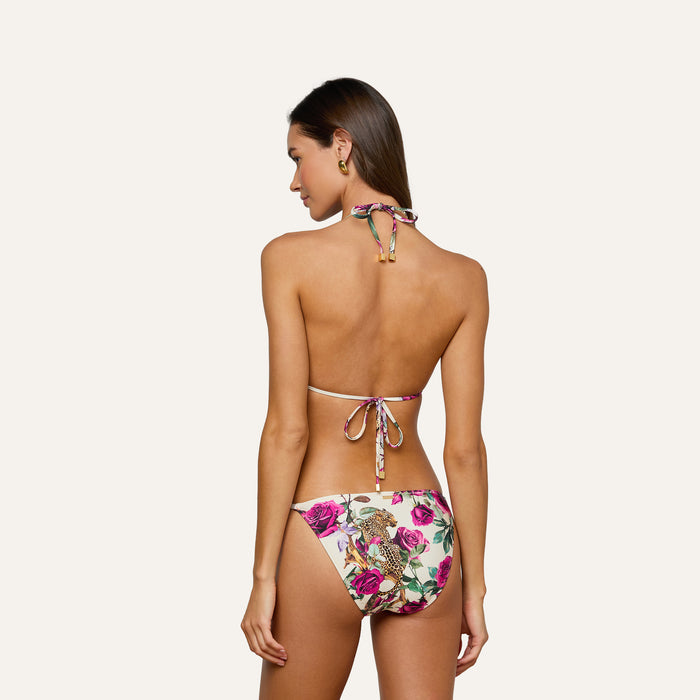 A woman stands facing away, wearing the Annabelle Triangle Bikini Top and matching jungle leopard print bottoms. The bikini top features a triangle silhouette and ties at the neck and back. She has long brown hair and small hoop earrings.
