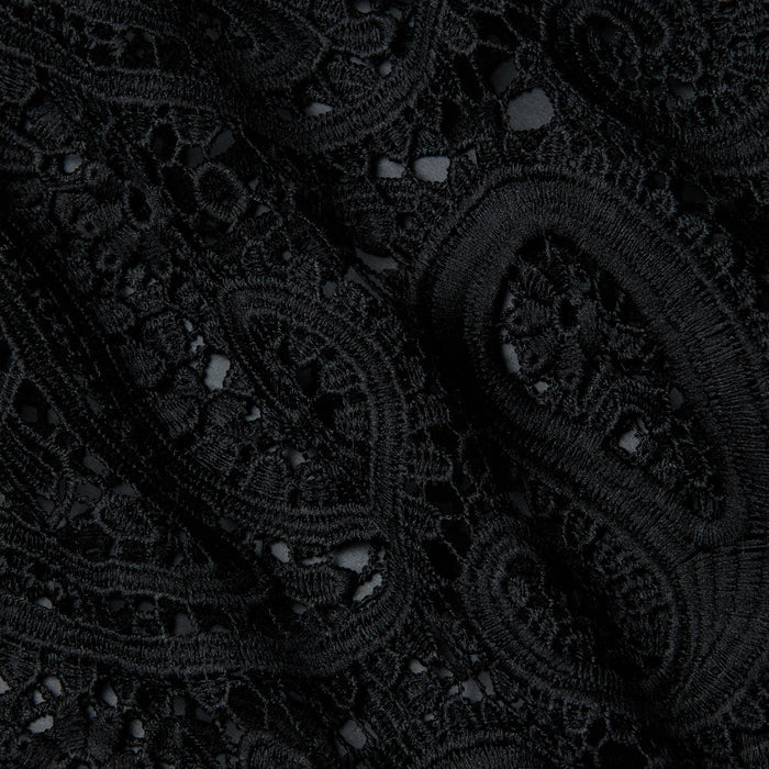Close-up of the Ansley Cover-Up Dress, featuring intricate black lace fabric with swirling paisley and floral patterns, showcasing textured embroidery and delicate openwork details reminiscent of boho style.