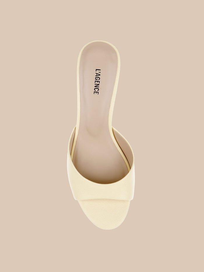 A single Arleen Kitten-Heel Mule in cream, featuring an open toe, a wide strap, and the LAGENCE logo on the insole, with a subtle kitten heel, displayed on a beige background.